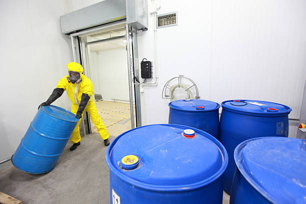 Worker in protective uniform,mask,gloves and boots rolling barrel of chemicals